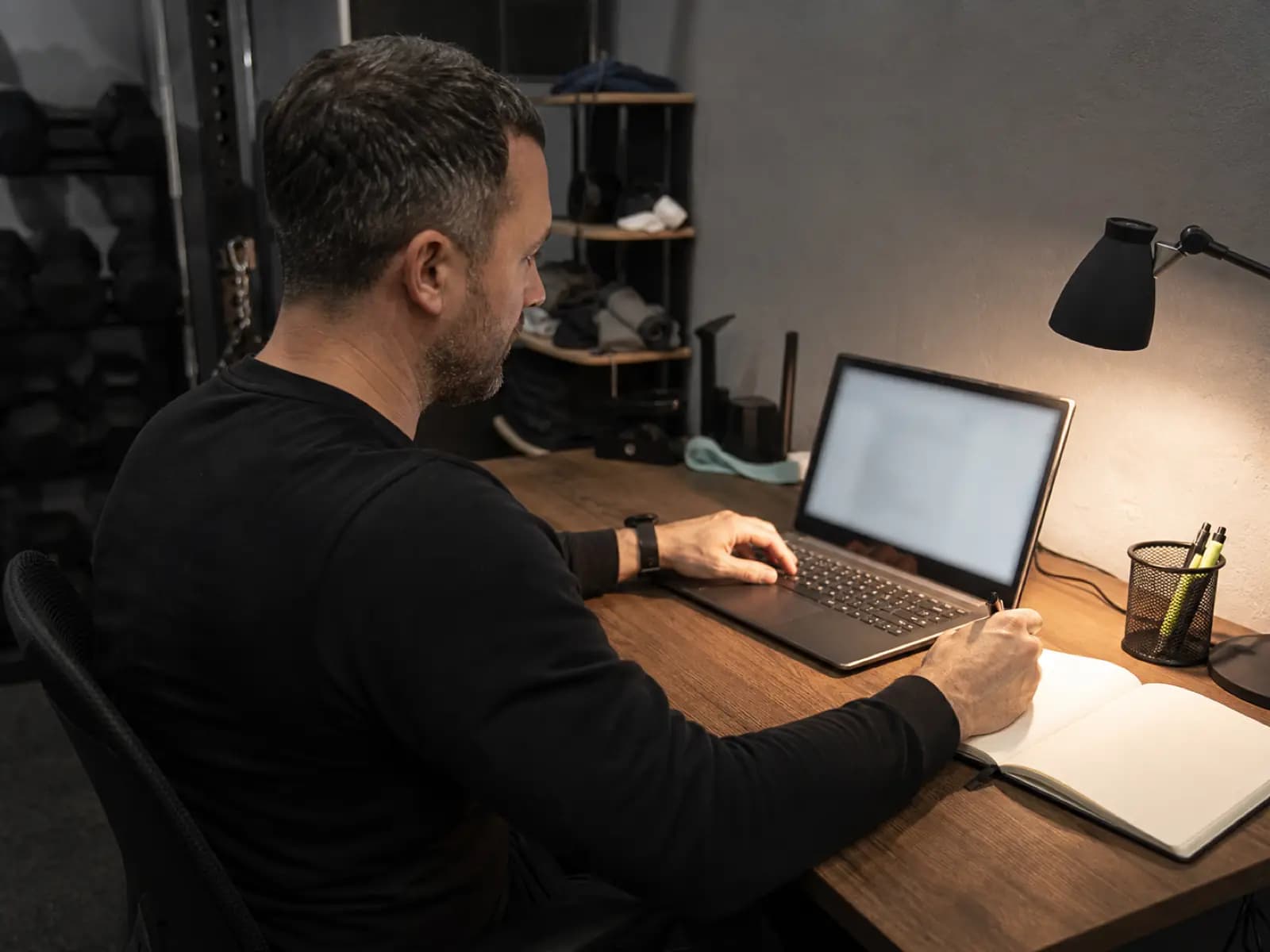 Trener pracuje wieczorem przy laptopie i notatniku