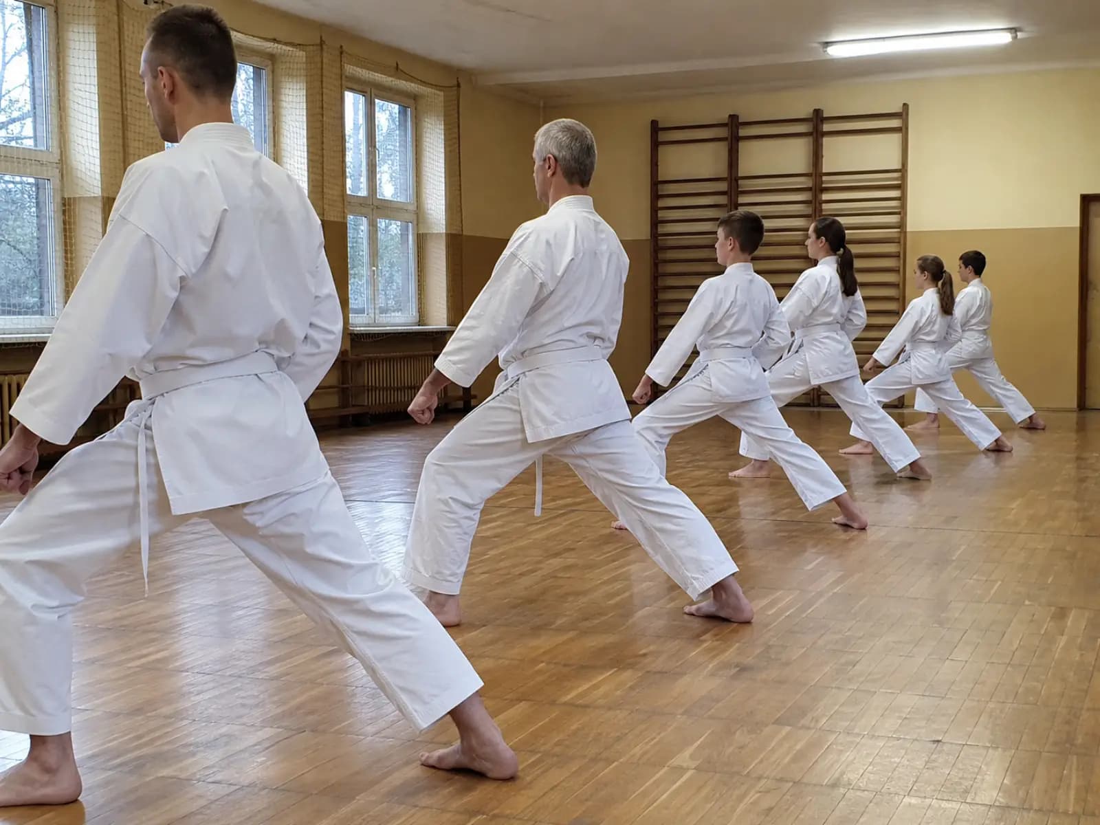 Grupa ćwiczy pozycję zenkutsu-dachi w sali karate